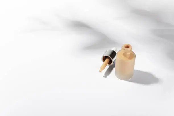 Liquid foundation cream bottle with pipette. Unbranded glass flacon of correction cosmetic product on light backdrop. Beauty and cosmetology branding concept. Copy space in left side.