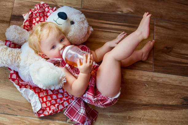 Baby bottle with milk and a measuring scale on the background of a lot of full bottles of breast milk with teddy bear and diaper. Mother's milk - the most healthy food for newborn,newborn equipment