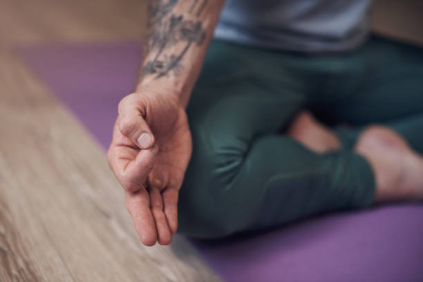 Becoming one with universal energy Cropped shot of an unrecognizable man sitting indoors alone and meditating with his hand in a gyan mudra man yoga tattoo stock pictures, royalty-free photos & images