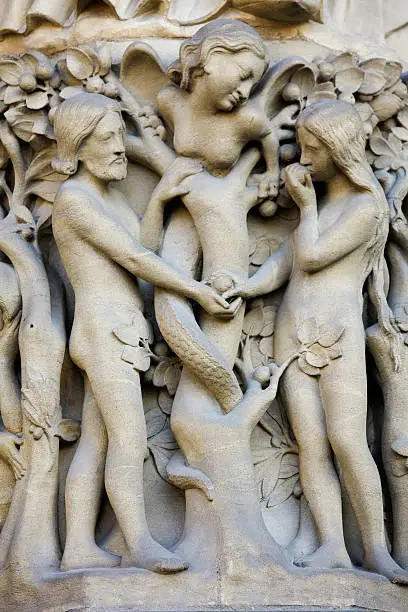 Adam, Eve and Lilith, the female serpent, in the garden of Eden. Eve eats the forbidden fruit. This statue was created in the 13th Century and is located at the entrance portal of the Notre Dame cathedral in Paris.