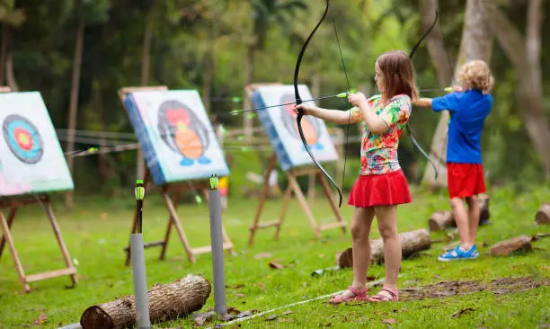 Archery for child. Little girl with bow and arrow. Kids shoot on tropical island. Target on outdoor shooting range. Archer club for young children. Healthy summer activity.