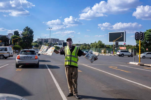 Newspaper street vendor in Sandton African senior selling newspapers at a busy intersection in Sandton City, Sandton houses approximately 300 000 residents and 10 000 businesses, including investment banks, top businesses, financial consultants, the Johannesburg stock exchange and one of the biggest convention centres on the African continent, the Sandton Convention Centre. newspaper seller stock pictures, royalty-free photos & images