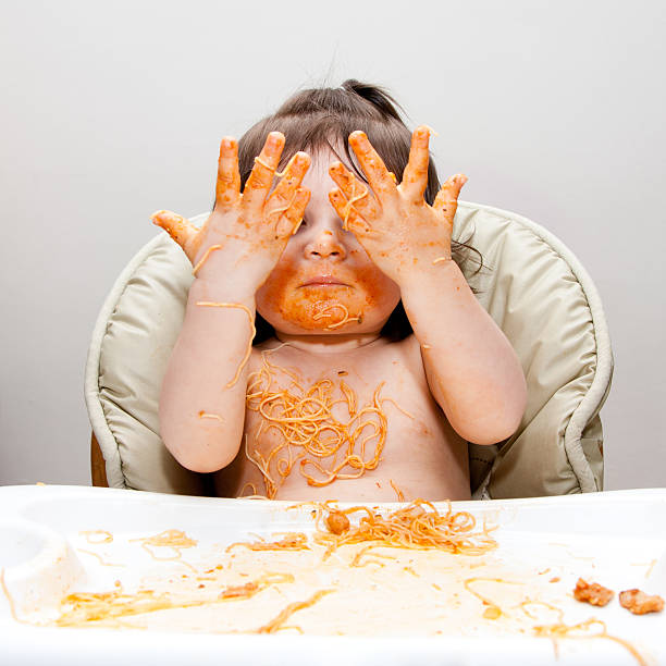 Happy funny messy eater Happy baby having fun eating messy showing hands covered in Spaghetti Angel Hair Pasta red marinara tomato sauce. kids eating noodles stock pictures, royalty-free photos & images