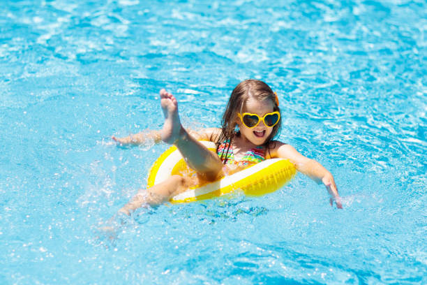 Child in swimming pool on ring toy. Kids swim. Child in swimming pool on inflatable yellow lemon ring. Little girl learning to swim with orange float. Water toy for baby and toddler. Healthy outdoor sport activity for children. Kids beach fun. game resort pictures stock pictures, royalty-free photos & images