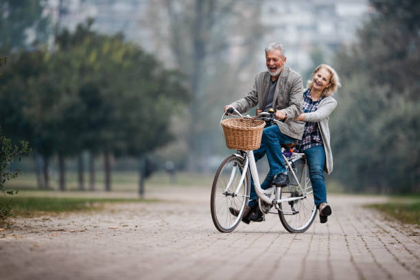 秋の日に自転車で楽しんでいる遊び心のある先輩カップル。 - retirement mature couple couple bicycle ストックフォトと画像