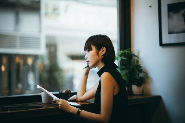 istock Thoughtful young Asian woman working over paperworks while having coffee in a cafe 1207011498