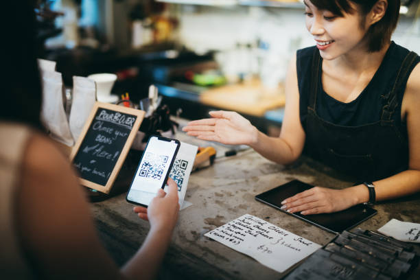 istock Customer scanning QR code, making a quick and easy contactless payment with her smartphone in a cafe in front of a smiling barista 1207011592