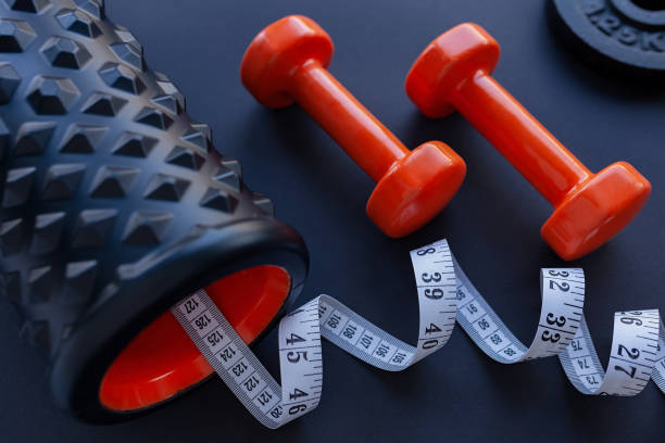 istock Two orange dumbbells with black bumpy foam roller and white tape measure on black background 1207012639