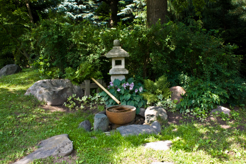 Part of Japanese garden in summer, with stone light, stones and plants.