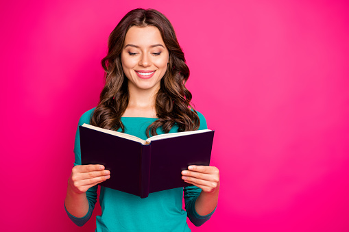Photo of cheerful positive nice cute charming girlfriend looking thorugh her copybook in search of answers to questions, she has smiling toothily isolated fuchsia color vivid background