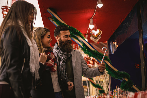 Low angle view of small group of friends walking by a stand of a Christmas market selecting the best candies to eat.