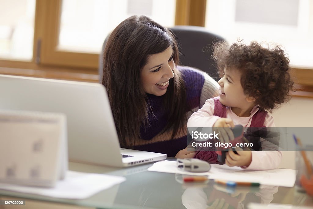 Multitasking mother with her daughter Mom and businesswoman working with laptop computer at home and playing with her baby girl. Horizontal shape, front view, waist up Child Stock Photo