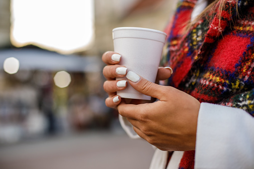 Cut out of delicate female hands using a styrofoam cup to drink hot beverage in a public area.