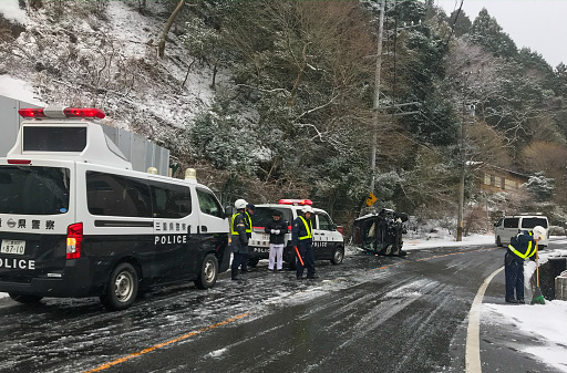 February 18 2020 in Komono, Mie prefecture, Japan a vehicle has flipped on its side while coming down an icy road early in the morning. Japans mountain roads can get very dangerous during the winter season. Police are on the scene to control traffic.