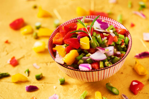 closeup of a bowl with a mix of different raw chopped vegetables, such as asparagus, onion, or yellow and red bell pepper, on a golden textured surface