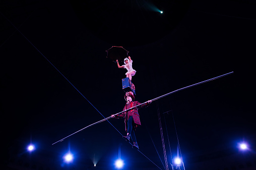 low angle view of man holding pole and supporting attractive acrobat while walking on rope