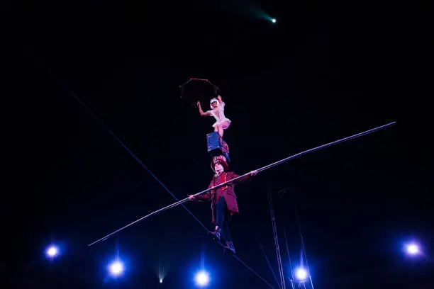 Photo of low angle view of man holding pole and supporting attractive acrobat while walking on rope