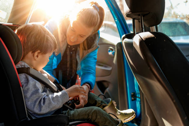 Mother putting her son in a car with his car safety seat Young mother putting her little boy in the car seat, fastening seat belts. adjusting seat stock pictures, royalty-free photos & images