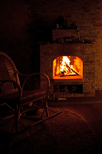 Rocking chair by the fireplace in a rustic house. Cozy evening by the fireplace.