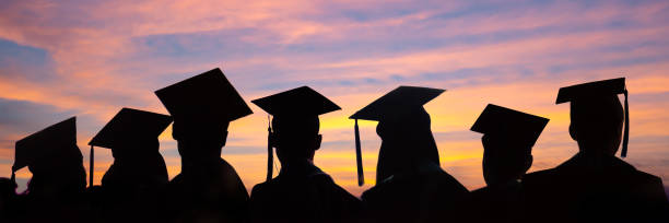 silhouettes des étudiants avec des chapeaux gradués dans une ligne sur le fond de coucher du soleil. cérémonie de remise des diplômes à la bannière web de l’université. - graduation color image people photography photos et images de collection