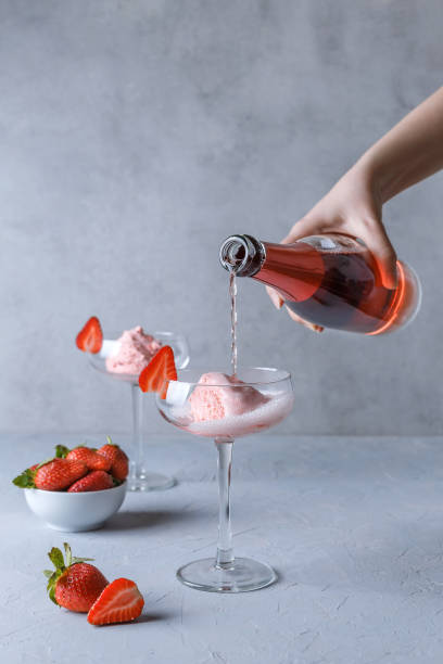 hand gießt rosa champagner in ein glas mit erdbeereis auf grauem hintergrund. das konzept der köstlichen getränke. - champagne pink strawberry champaigne stock-fotos und bilder