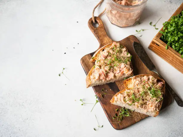 Healthy toasts with salmon pate and fresh green sprouts on yeast-free bread on wood cutting board