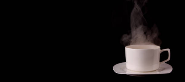 istock White coffee cup on plate with smoke isolated on black background in studio With copy space. 1207037734