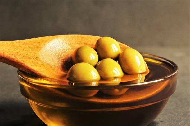 ciotola di olio d'oliva cucchiaio di legno e oliva verde in cima - cooking oil olive oil nutritional supplement spoon foto e immagini stock