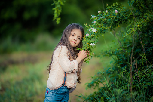 Close up of a girl with long brown hair near a green Bush with white flowers