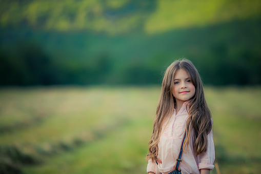 Close up of a child in a pink blouse with long dark hair in an open field