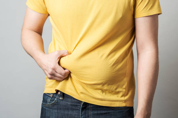 primer plano de la mano del hombre obeso con sobrepeso sosteniendo su gran vientre aislado sobre fondo gris - abdomen humano fotografías e imágenes de stock