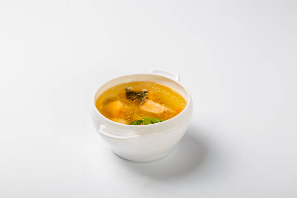 istock Fish soup with salmon. A white round plate is filled with a transparent broth, which shows pieces of salmon, potatoes and greens. Plate on a white background. Side view 1207045356