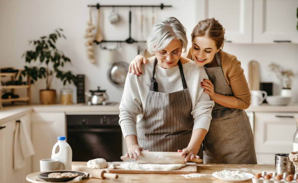 glückliche familie großmutter alte mutter schwiegermutter und schwiegertochter tochter kochen in der küche, kneten teig, backen kekse - baking lifestyles beautiful cookie stock-fotos und bilder