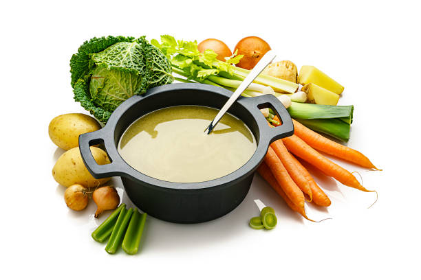High angle view of a black cooking pan filled with a healthy vegetables broth isolated on white background. Fresh multi colored vegetables like carrots, kale, potatoes, celery and onions are all around the pan. High resolution 42Mp studio digital capture taken with Sony A7rii and Sony FE 90mm f2.8 macro G OSS lens