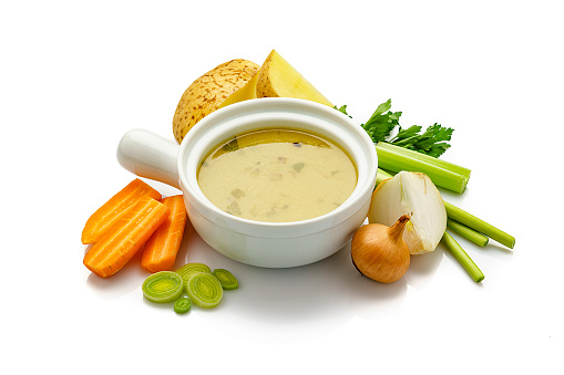 High angle view of a white bowl filled with a healthy vegetables broth isolated on white background. Fresh multi colored vegetables like carrots, kale, potatoes, celery and onions are all around the bowl. High resolution 42Mp studio digital capture taken with Sony A7rii and Sony FE 90mm f2.8 macro G OSS lens