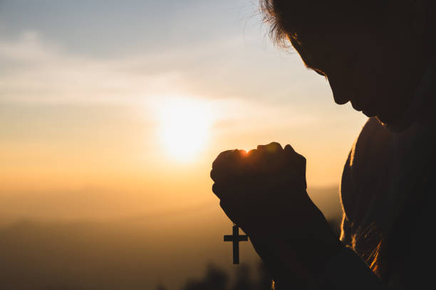 silhouette der junge menschliche hände betend mit einem kreuz bei sonnenaufgang, christian religion konzept hintergrund. - praying men god kneeling stock-fotos und bilder