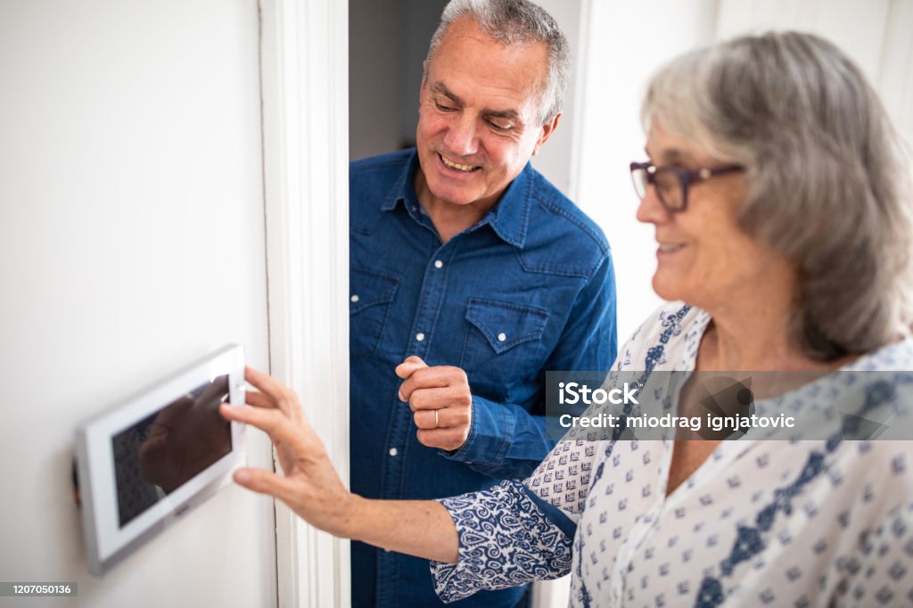 Senior man explaining to his wife how to set burglar alarm Senior man explaining to his wife how to set burglar alarm at home Burglar Alarm Stock Photo