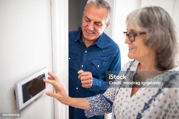 Senior Man Explaining To His Wife How To Set Burglar Alarm Stock Photo - Download Image Now