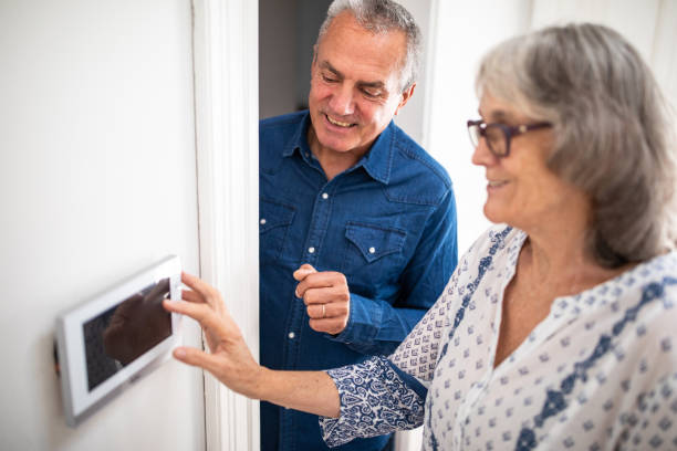 senior man explaining to his wife how to set burglar alarm - security system security burglar alarm residential structure imagens e fotografias de stock