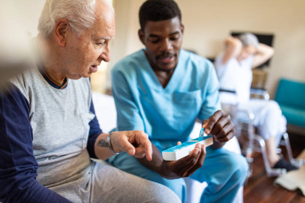 schwarze männliche krankenschwester gibt anweisungen an senior-patienten, wenn seine pillen zu nehmen - senior adult old nursing home people stock-fotos und bilder