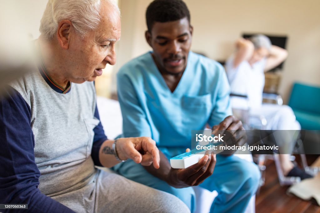 Black male nurse giving instructions to senior patient when to take his pills Black male nurse sitting on bed and giving instructions to senior patient when to take his pills in nursing home Senior Adult Stock Photo