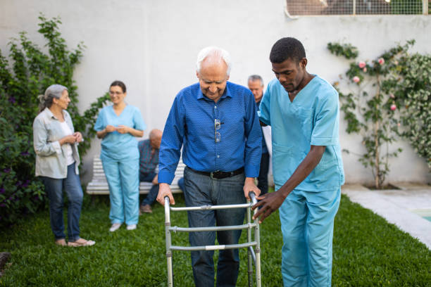 So proud of your progress Black Male nurse helping senior man with mobility walker outdoor on beautiful day in backyard of nursing home walking aide stock pictures, royalty-free photos & images