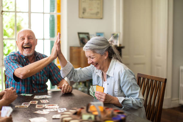 I knew that we can win this Group of senior friends sitting at dining table playing cards together and having good time at home friends playing cards stock pictures, royalty-free photos & images