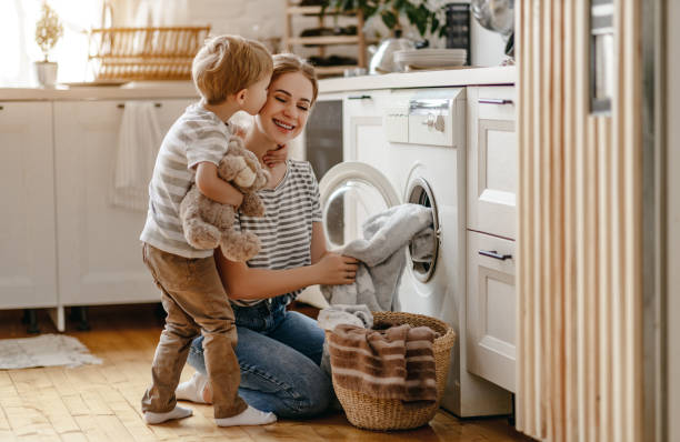 feliz familia madre ama de casa y el niño en la lavandería con lavadora - stereotypical housewife little girls family domestic kitchen fotografías e imágenes de stock