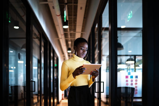 junge geschäftsfrau zu fuß und mit digitalen tablet im korridor büro - people office mobility looking stock-fotos und bilder