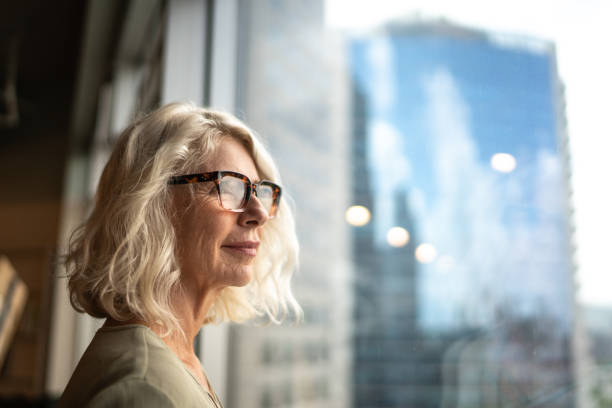 femme d’affaires mûr regardant par la fenêtre - thinking women businesswoman business photos et images de collection