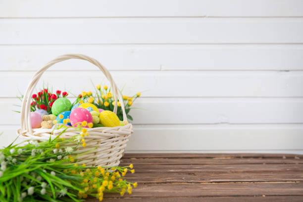 Colored easter eggs in the basket and spring flowers on wooden background. Greeting card.