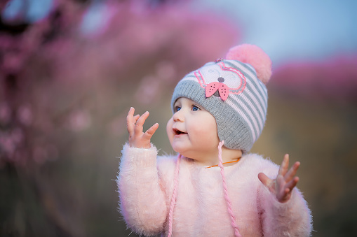 Cute girl in a pink hat with a bells in the garden with peach blossoming trees.