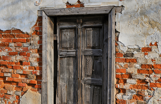 Window with closed green damaged wooden shutters,\npainted house wall with rough and cracked surface, no person, vertical format