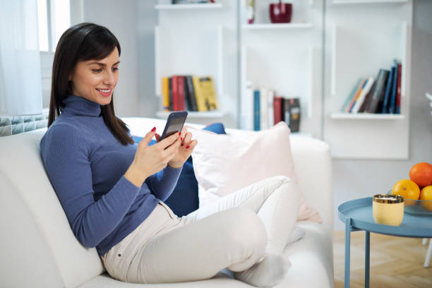 istock Young charming brunette sitting on couch in her beautiful home and typing message. 1207059192